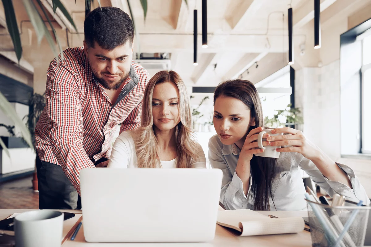 DevOps tým tří mladých lidí, kteří se dívají do jednoho notebooku