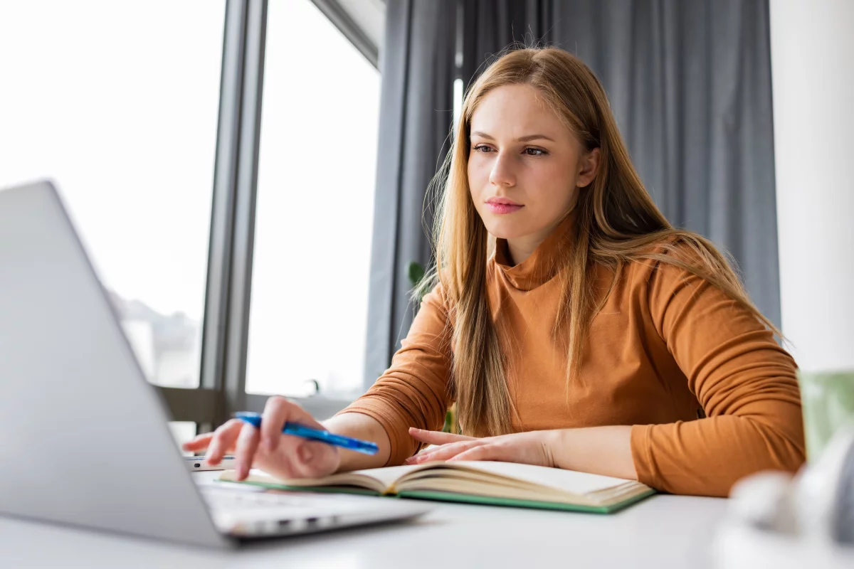 Mladá žena hledá práci na notebooku a píše motivační list.